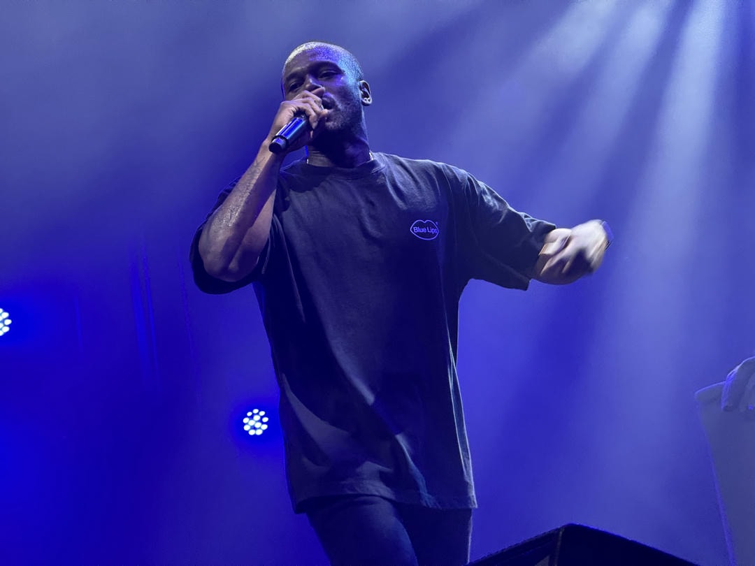 ScHoolboy Q performing live on stage. He's holding the microphone up to his mouth and is shrouded in blue light