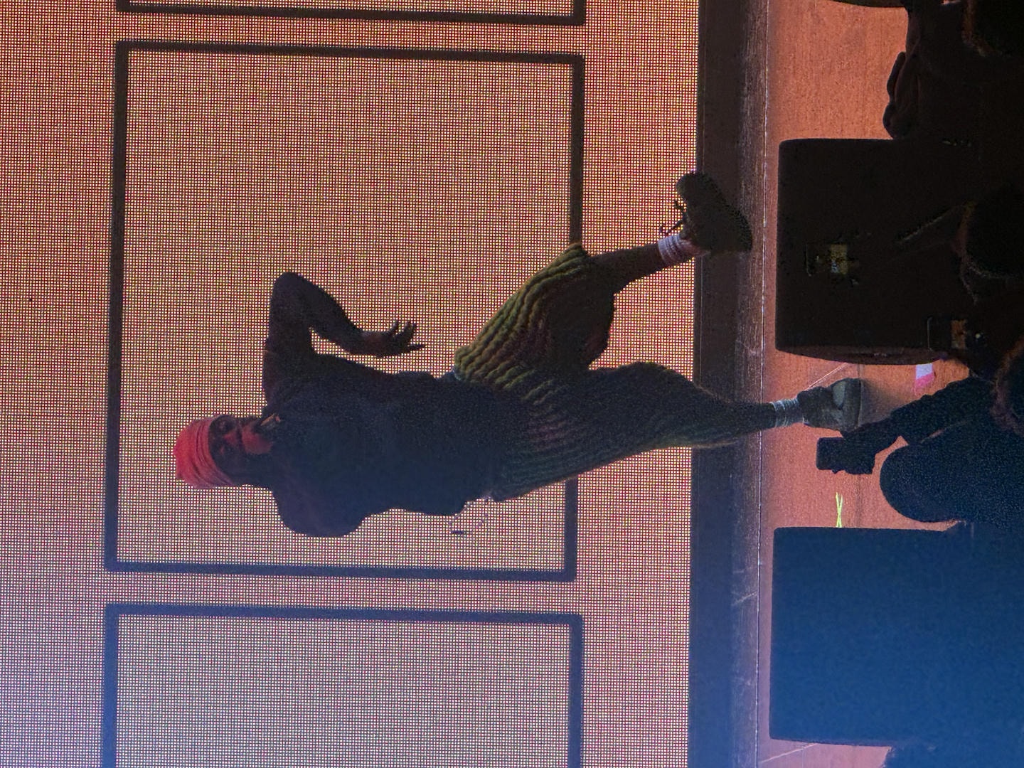 Aminé jumping on stage while performing. He's backlit by a big LED screen behind him.