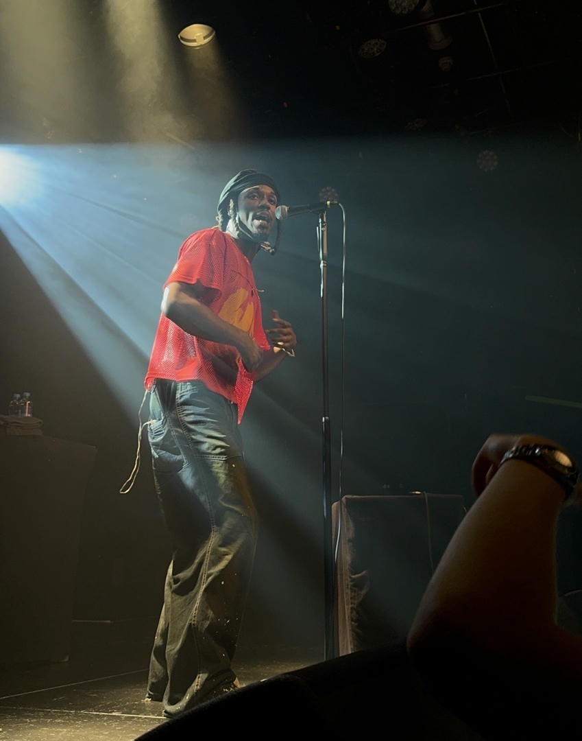 Saba backlit by a spotlight on stage, singing into a microphone