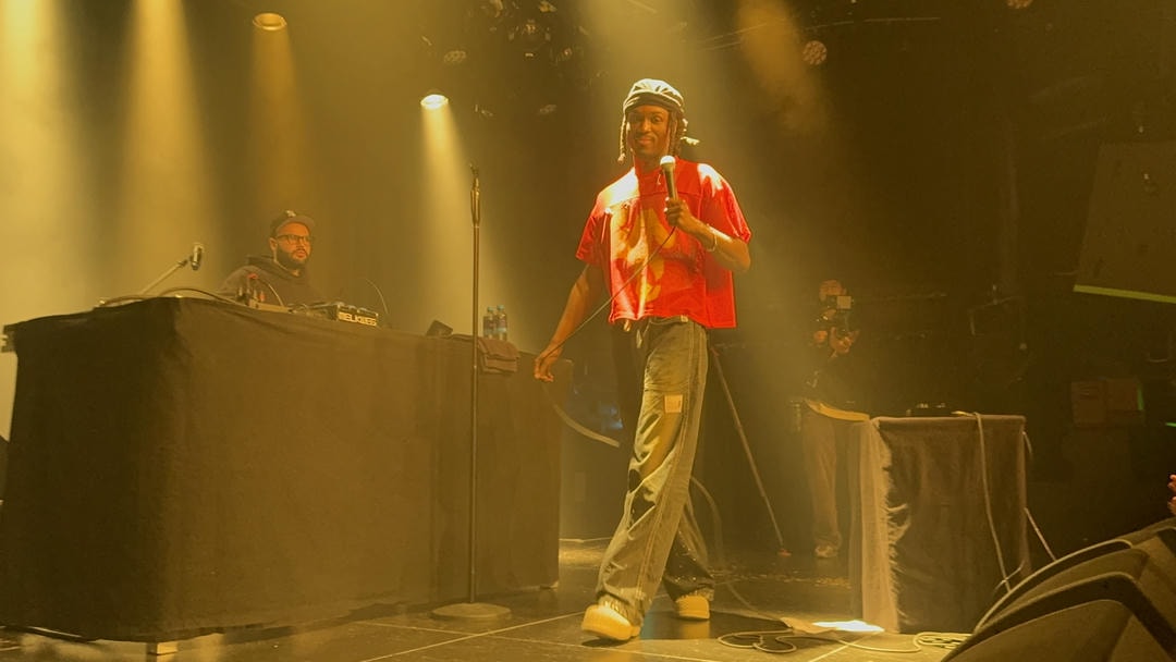 Saba in yellow light, walking across the stage with a microphone in hand