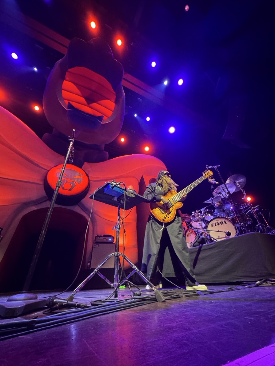 Thundercat on stage. Behind him is a massive inflatable cat, and next to him is his drummer behind a drumset
