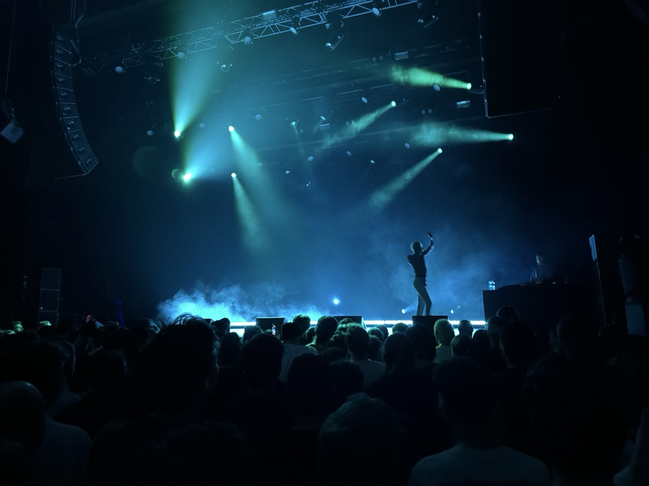 Wide shot of Danny Brown performing on stage. The crowd is visible in the foreground and the stage Danny is on is lit by a bunch of blue and teal lights.