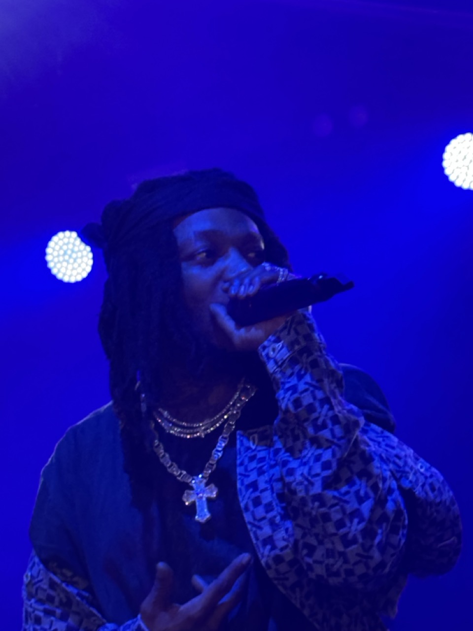 Close-up of JID with the mic up to his face performing on stage. He's lit by blue lights behind him.