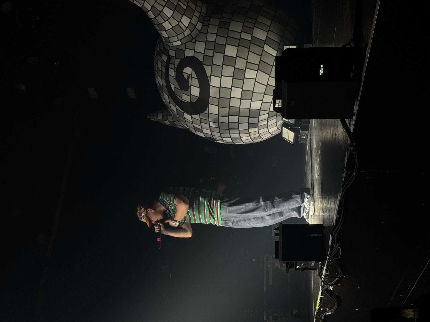 Brae on stage, singing into the microphone. He's lit by a single spotlight.