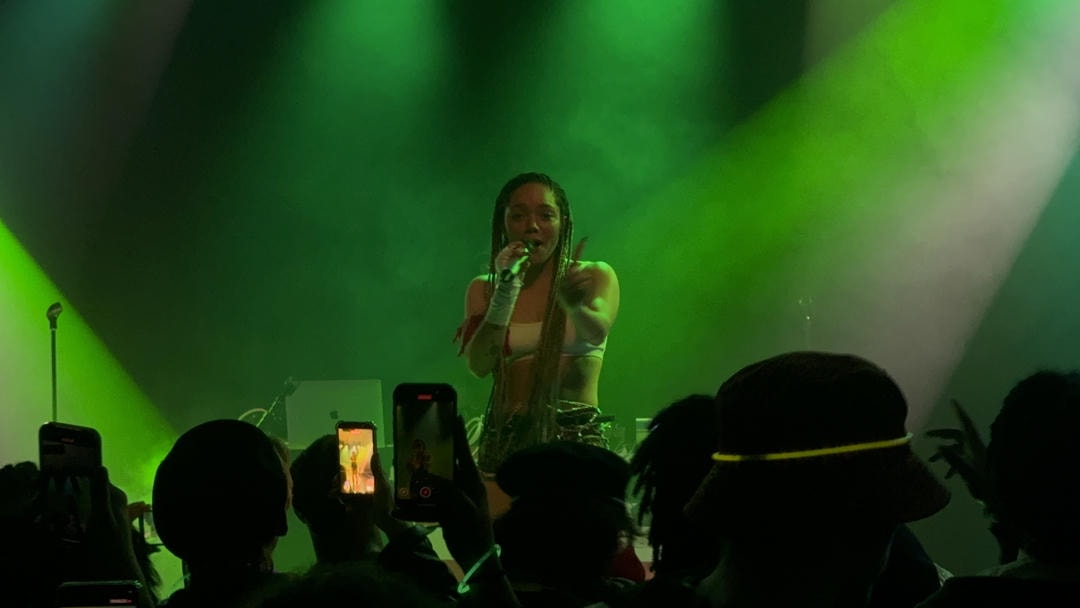 Jadagrace performing on stage, surrounded by green spotlights. In the foreground you can see a crowd of people watching her.
