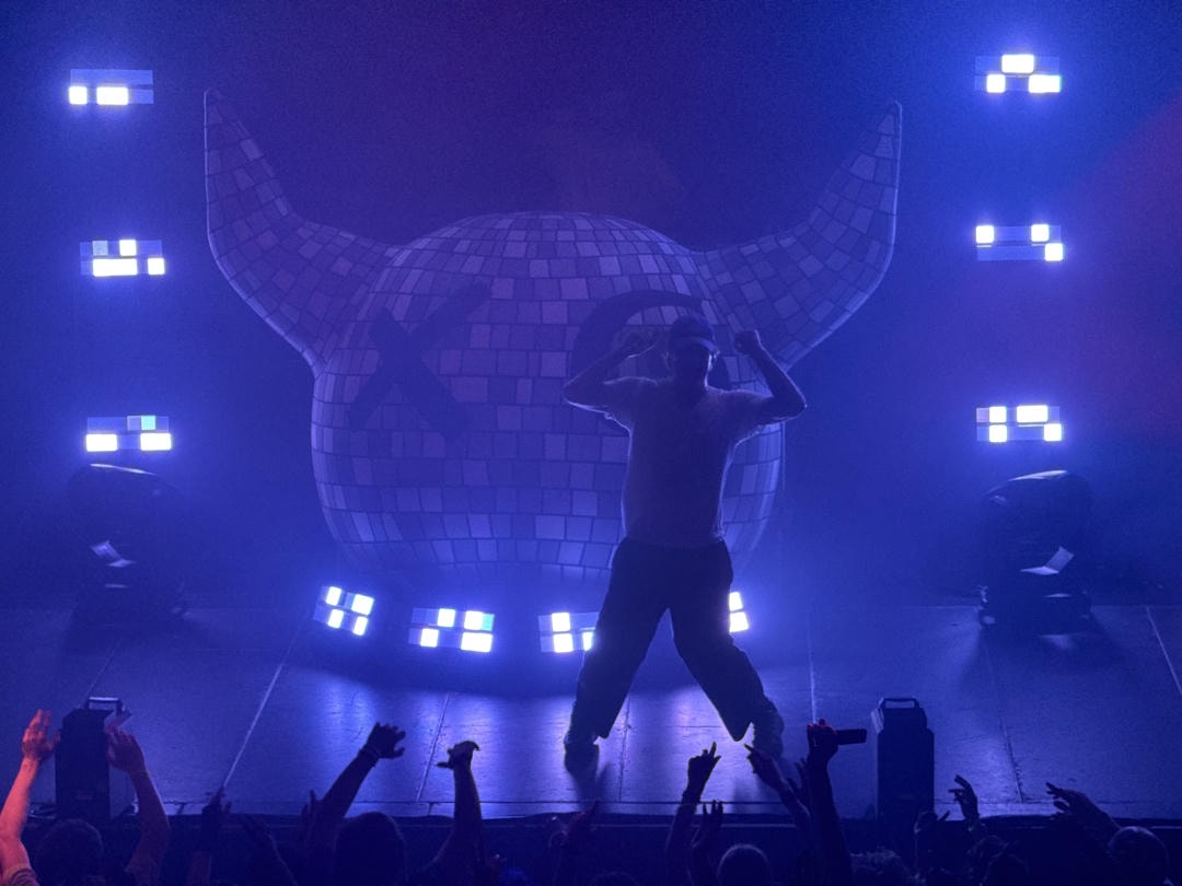 Joey Valence is seen backlit by some blue LED lights in front of JVB's iconic blow-up balloon.