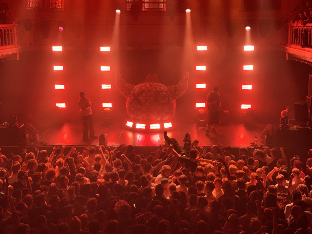 Joey Valence & Brae performing live on stage. The crowd is seen from up above, with one person being crowd-surfed to the front.
