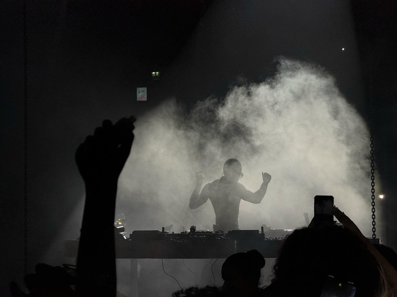 A silhouette of Kaytranada can be seen dancing behind a DJ booth. Some of the audience's hands in the air can be seen in the foreground