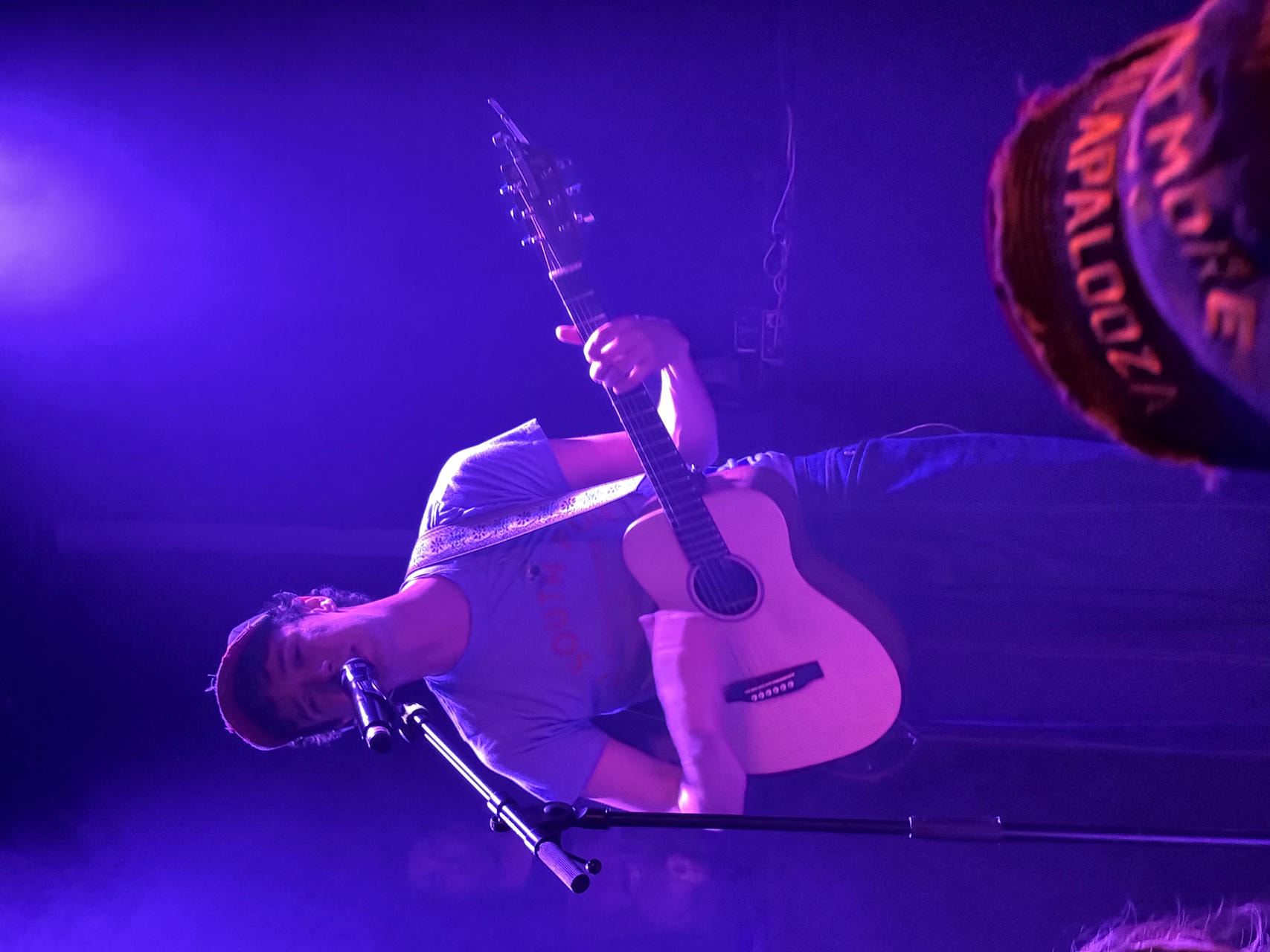 Jackson August of WHATMORE playing the acoustic guitar and singing into the microphone on stage.