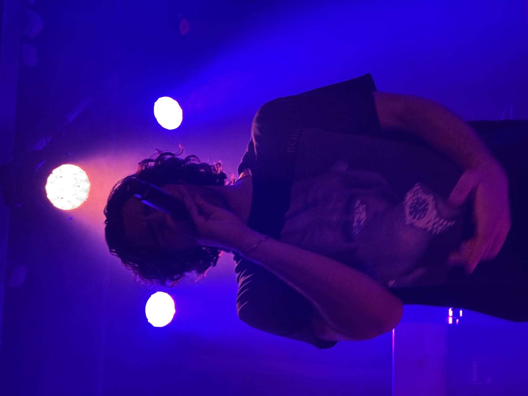 Sebastiano of WHATMORE singing into the microphone on stage. He's backlit and appeares like a silhouette.