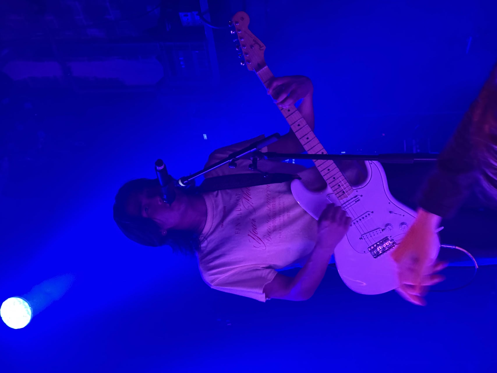 Yoshi T. of WHATMORE playing the electric guitar and singing into the microphone on stage.