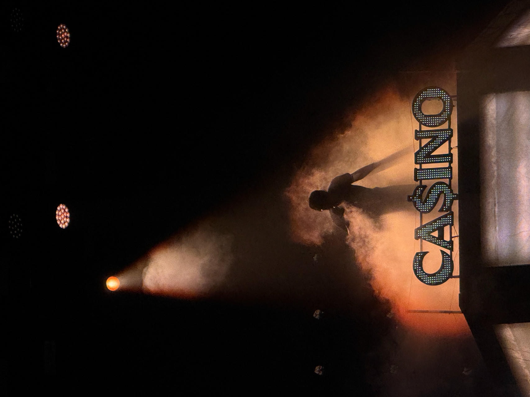 Baby Keem performing on stage. He's surrounded by smoke, backlit by an orange spotlight. He's standing in front of a sign that says 'CA$INO'.