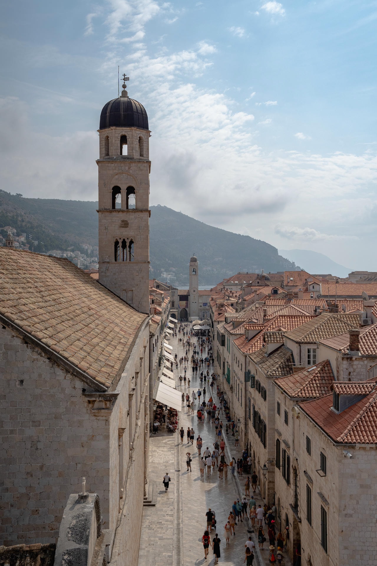 An alley in Dubrovnik, photographed from above. A tower stands tall on the left side of the foot traffic in the alley.