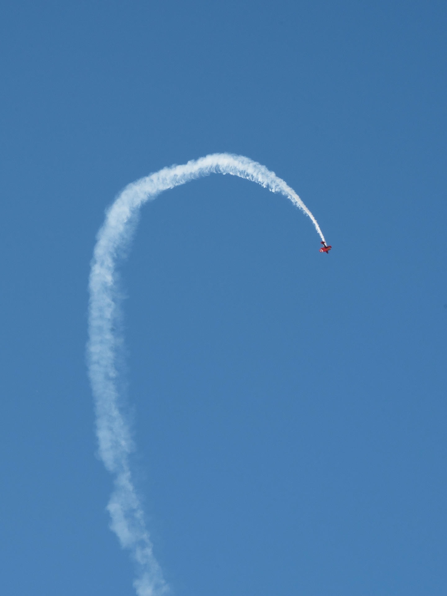 A red airplane about 70% through a backflip. A trail of smoke is trailing behind.